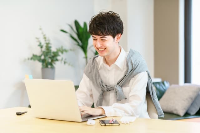 カーディガンを羽織りPCを操作する男性の画像